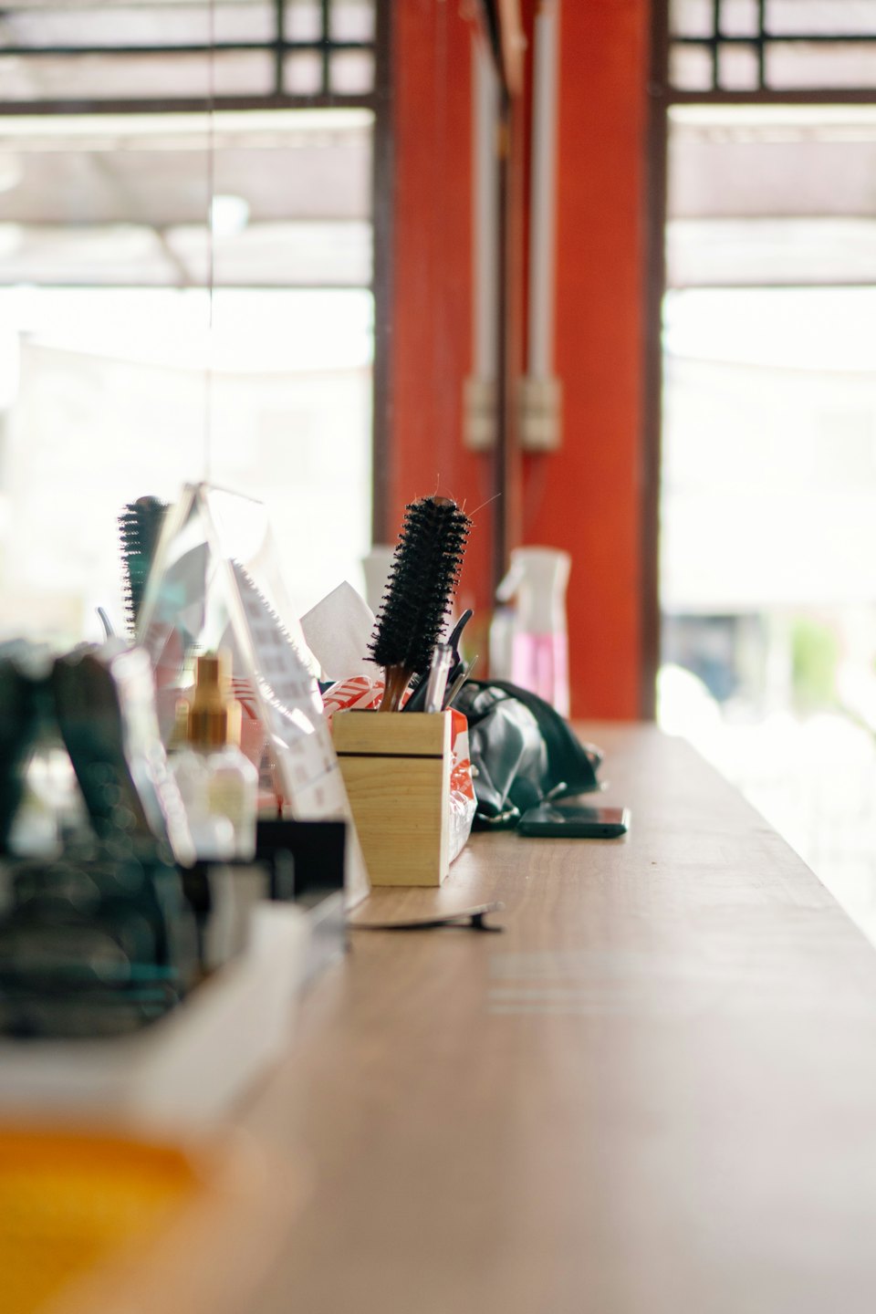 Attrezzi per parrucchiere, tra cui spazzola, forcine e flacone spray, su un bancone di legno.