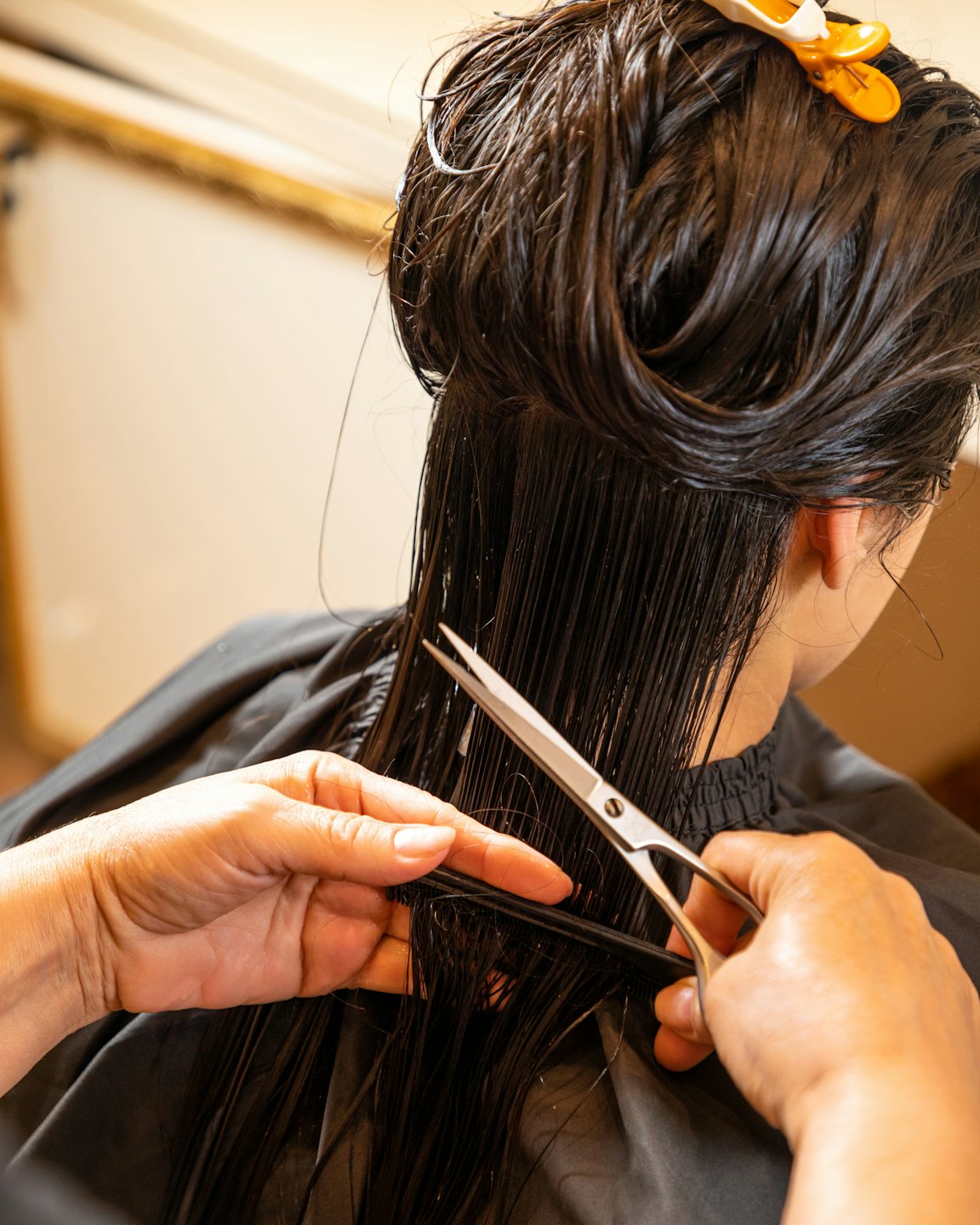 Parrucchiere taglia i capelli scuri e bagnati di una cliente in un salone.