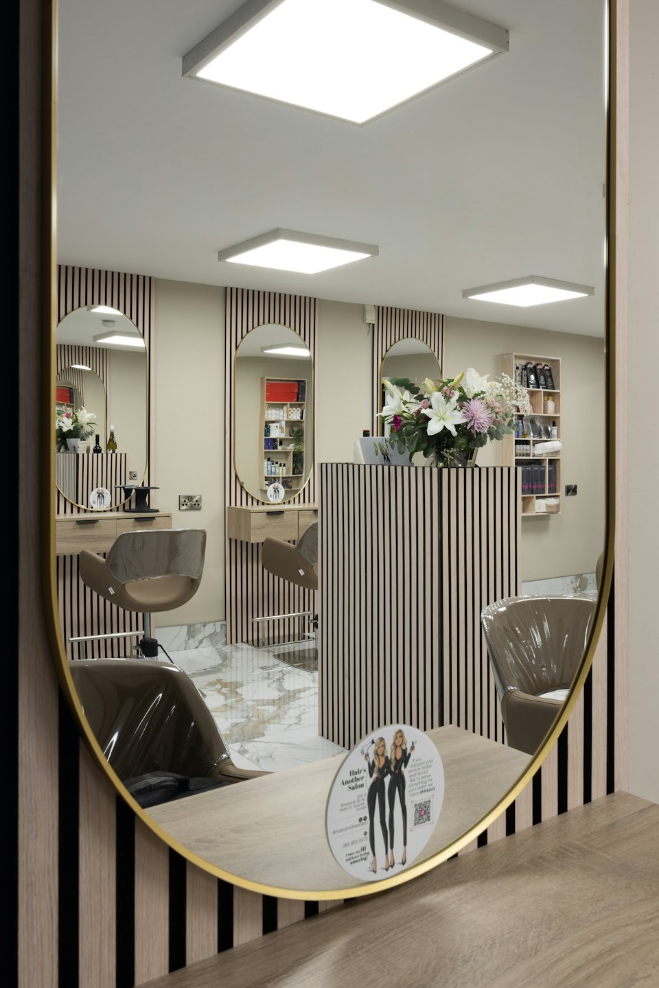 Interno di un moderno salone di parrucchiere riflesso in un grande specchio con cornice dorata.